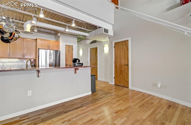 kitchen featuring a high ceiling, a kitchen breakfast bar, decorative backsplash, stainless steel fridge, and light hardwood / wood-style floors