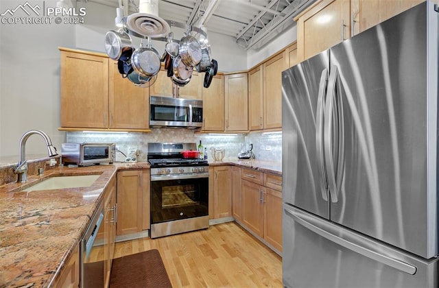 kitchen with sink, tasteful backsplash, light stone counters, light hardwood / wood-style floors, and appliances with stainless steel finishes