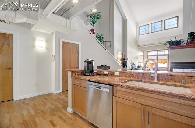 kitchen featuring dishwasher, sink, a high ceiling, light stone counters, and light hardwood / wood-style floors