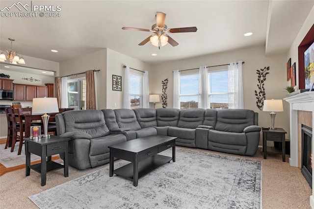 carpeted living room featuring a tiled fireplace and ceiling fan with notable chandelier