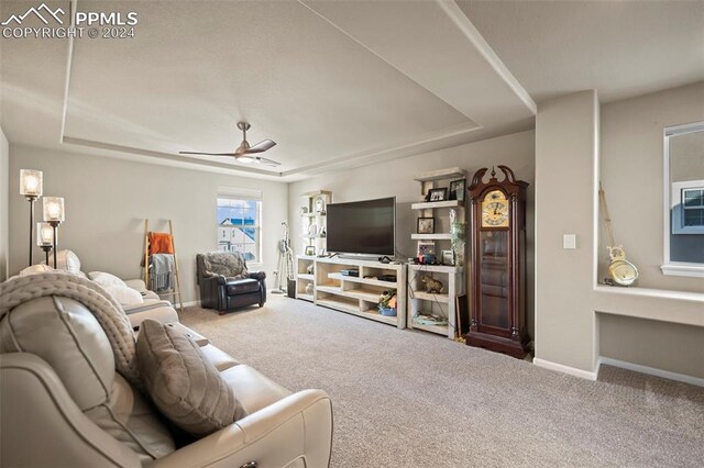 carpeted living room with ceiling fan and a raised ceiling