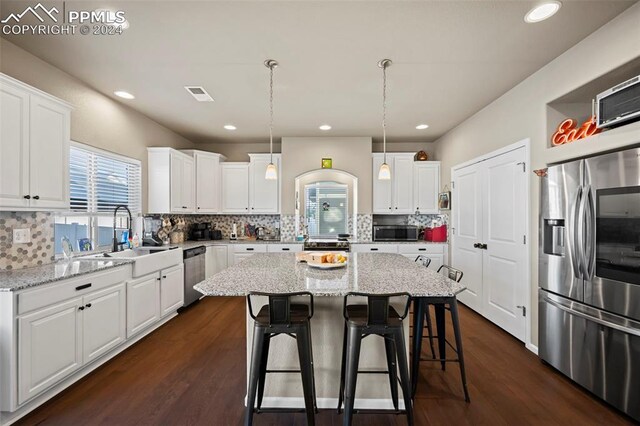 kitchen with white cabinetry, a center island, dark hardwood / wood-style floors, pendant lighting, and appliances with stainless steel finishes