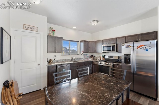 kitchen with appliances with stainless steel finishes, dark brown cabinetry, dark hardwood / wood-style flooring, and dark stone counters