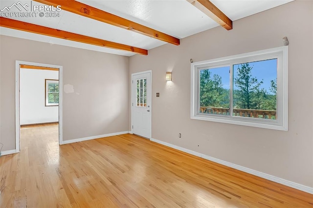 unfurnished room featuring beamed ceiling, light hardwood / wood-style floors, and plenty of natural light