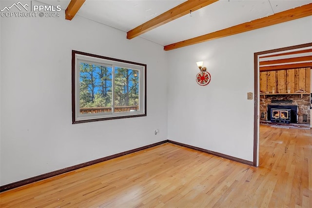 spare room with beamed ceiling, light hardwood / wood-style floors, and a wood stove