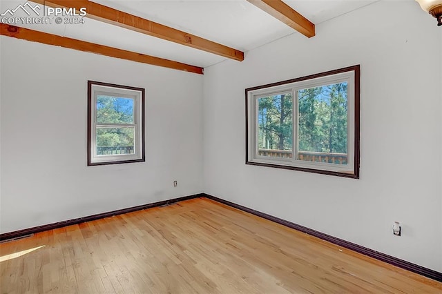 empty room with a healthy amount of sunlight, light wood-type flooring, and beam ceiling