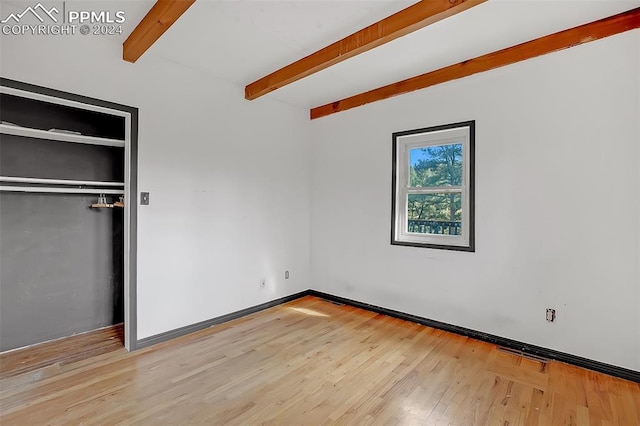 unfurnished bedroom with beamed ceiling and light hardwood / wood-style floors