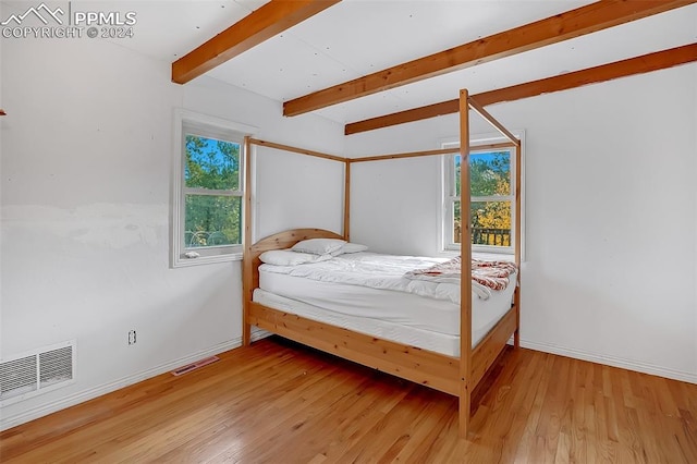 bedroom with multiple windows, beamed ceiling, and wood-type flooring