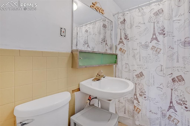 bathroom with toilet, curtained shower, sink, and tile walls