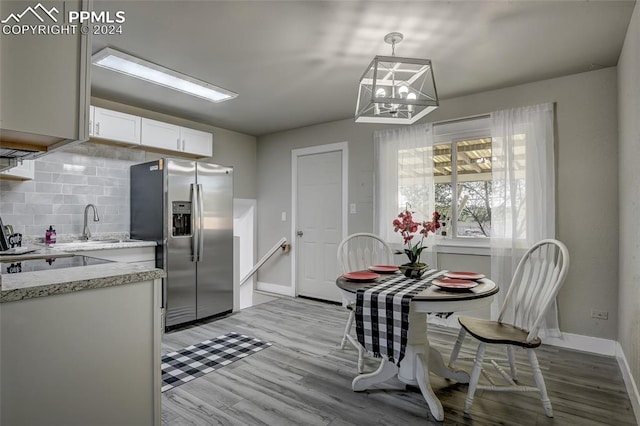 kitchen featuring white cabinets, stainless steel refrigerator with ice dispenser, hanging light fixtures, light wood-type flooring, and tasteful backsplash