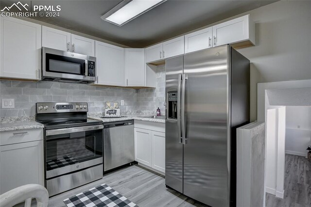 kitchen with stainless steel appliances, white cabinetry, and light hardwood / wood-style floors