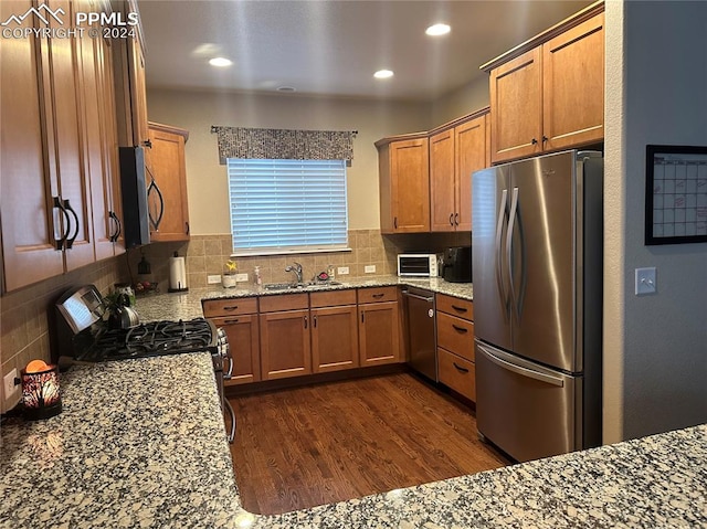 kitchen with light stone countertops, sink, stainless steel appliances, dark hardwood / wood-style floors, and backsplash