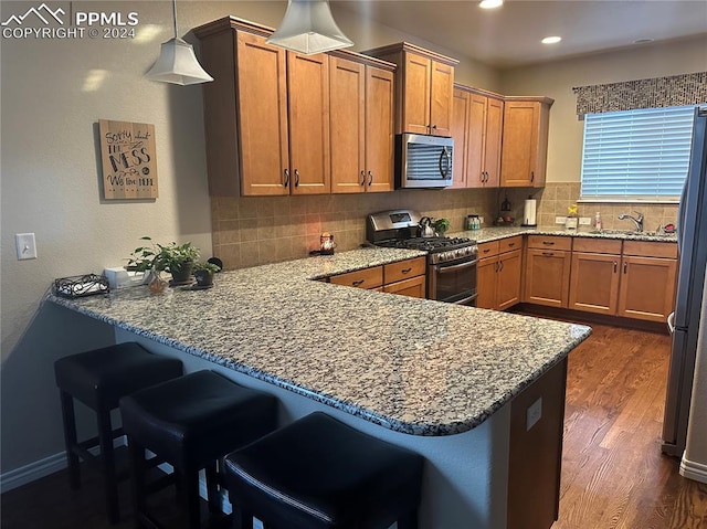 kitchen with pendant lighting, appliances with stainless steel finishes, tasteful backsplash, dark hardwood / wood-style flooring, and kitchen peninsula