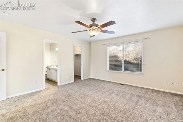 unfurnished bedroom with light carpet, a walk in closet, ensuite bathroom, ceiling fan, and a closet