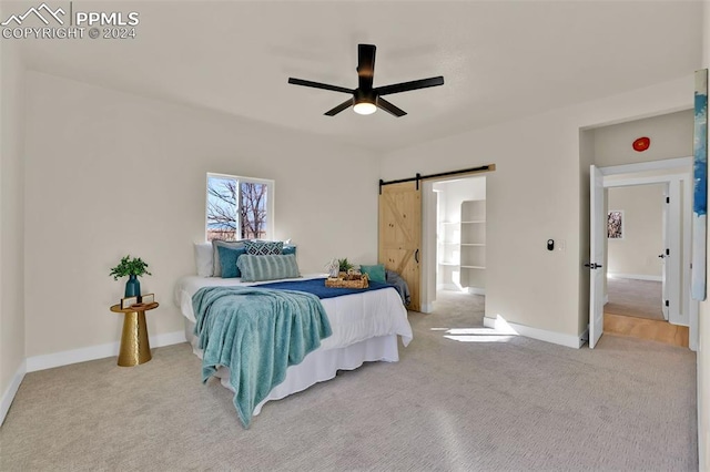 carpeted bedroom with a barn door and ceiling fan