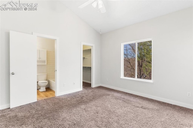 unfurnished bedroom with a walk in closet, light colored carpet, ceiling fan, connected bathroom, and lofted ceiling