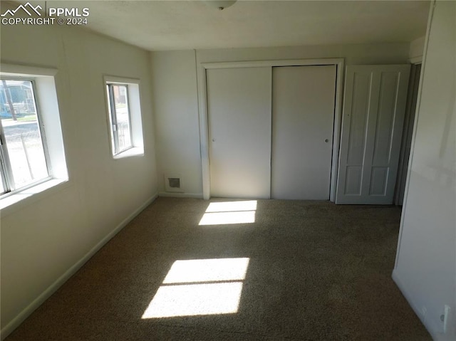 unfurnished bedroom featuring dark colored carpet, a closet, and multiple windows