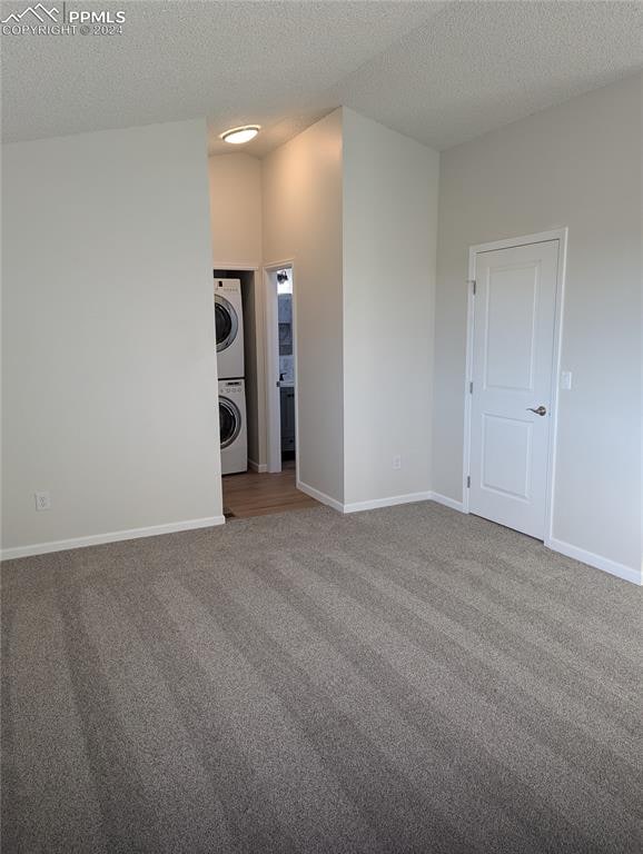 carpeted spare room featuring stacked washer / dryer and a textured ceiling