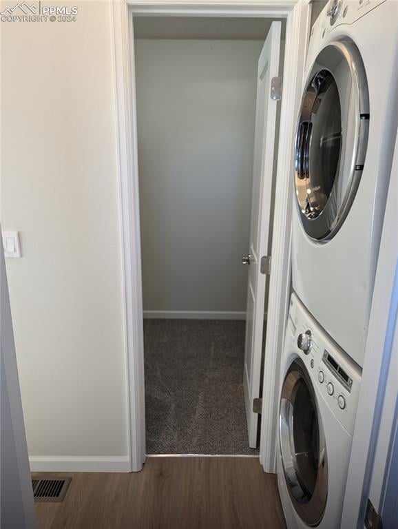 laundry room with dark wood-type flooring and stacked washer and clothes dryer