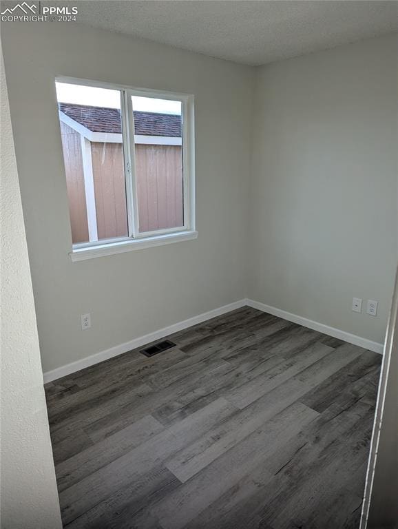 spare room featuring a textured ceiling and dark hardwood / wood-style flooring