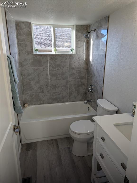 full bathroom featuring vanity, a textured ceiling, hardwood / wood-style floors, toilet, and tiled shower / bath