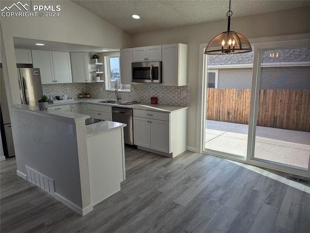 kitchen with vaulted ceiling, white cabinets, stainless steel appliances, and decorative light fixtures