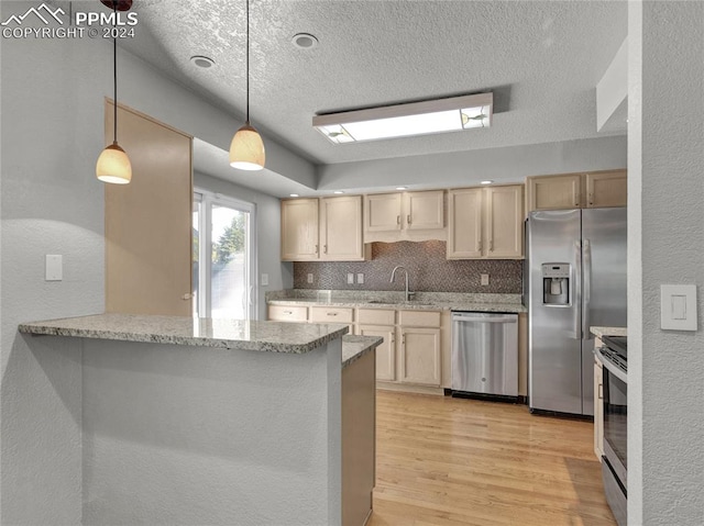 kitchen featuring backsplash, hanging light fixtures, light wood-type flooring, appliances with stainless steel finishes, and kitchen peninsula