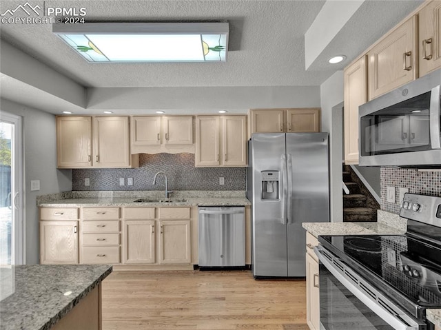 kitchen with sink, decorative backsplash, light stone countertops, light brown cabinetry, and appliances with stainless steel finishes