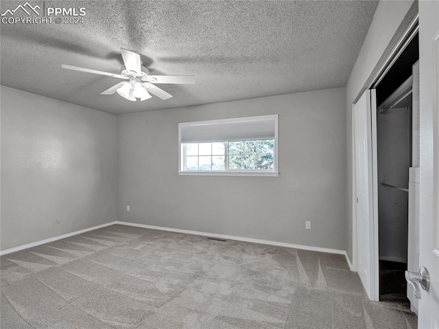 unfurnished bedroom featuring a closet, a textured ceiling, light colored carpet, and ceiling fan