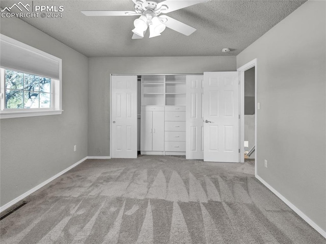 unfurnished bedroom featuring ceiling fan, a closet, light carpet, and a textured ceiling