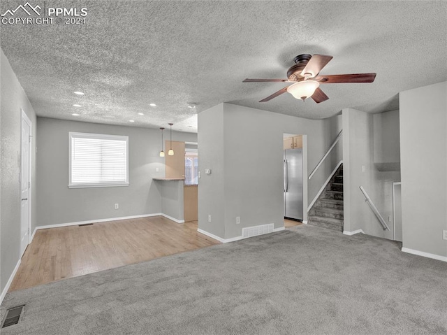 unfurnished living room featuring ceiling fan, a textured ceiling, and light hardwood / wood-style flooring