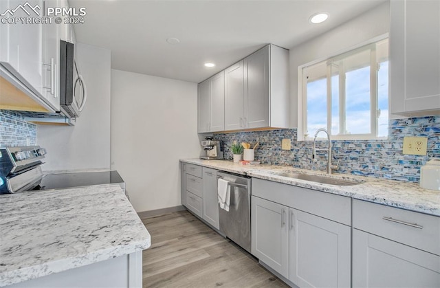 kitchen with backsplash, sink, light stone countertops, light hardwood / wood-style floors, and stainless steel appliances