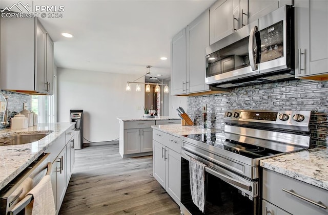 kitchen with decorative backsplash, appliances with stainless steel finishes, light wood-type flooring, and light stone counters