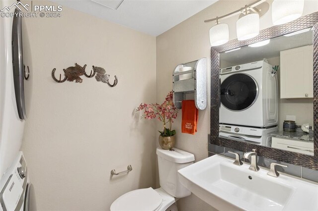 bathroom with stacked washer / drying machine, toilet, and sink