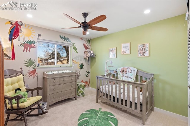 bedroom featuring light colored carpet, a nursery area, and ceiling fan