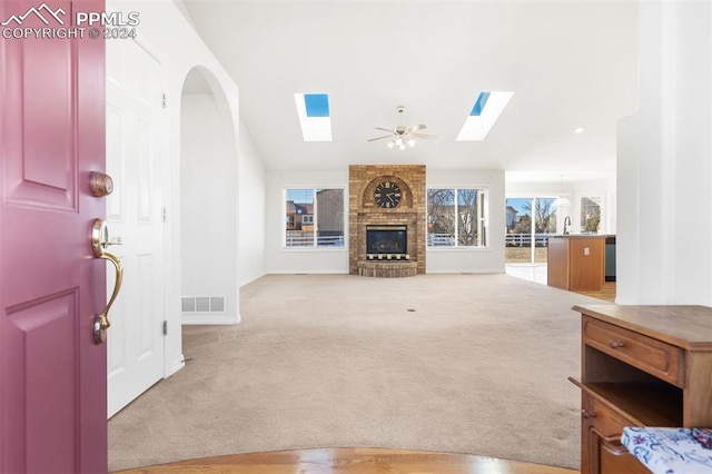 carpeted living room featuring ceiling fan, a skylight, sink, and a brick fireplace