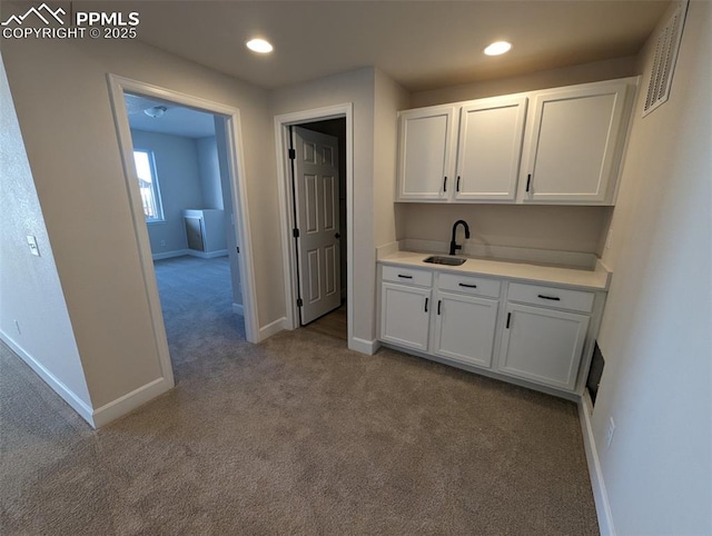 kitchen with sink, white cabinetry, light carpet, and washer / dryer