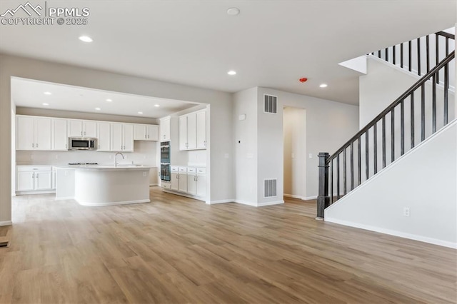 kitchen featuring white cabinetry, sink, a center island with sink, and light hardwood / wood-style flooring