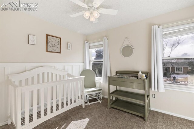 carpeted bedroom featuring a textured ceiling, a nursery area, and ceiling fan