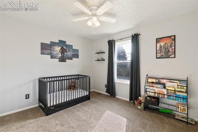 carpeted bedroom featuring ceiling fan, a crib, and a textured ceiling