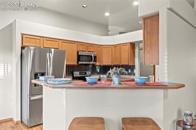 kitchen with decorative backsplash, kitchen peninsula, appliances with stainless steel finishes, and light hardwood / wood-style flooring