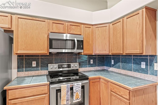 kitchen with backsplash, tile counters, light brown cabinets, and appliances with stainless steel finishes