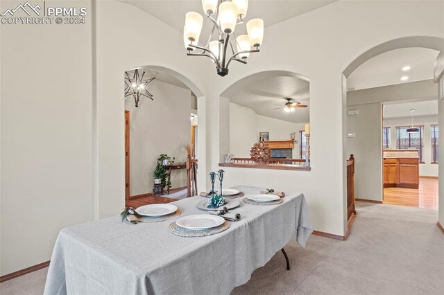 dining area with lofted ceiling, light carpet, and ceiling fan with notable chandelier