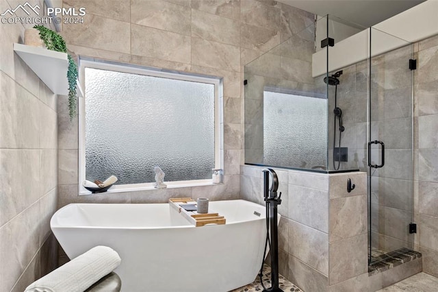 bathroom featuring plus walk in shower, tile walls, and a wealth of natural light