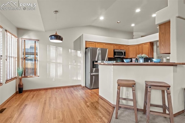 kitchen featuring kitchen peninsula, a kitchen bar, stainless steel appliances, light hardwood / wood-style floors, and hanging light fixtures