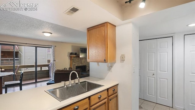 kitchen featuring a fireplace, sink, light tile patterned floors, and a textured ceiling