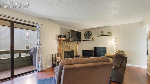 living room featuring a textured ceiling, hardwood / wood-style flooring, and a stone fireplace