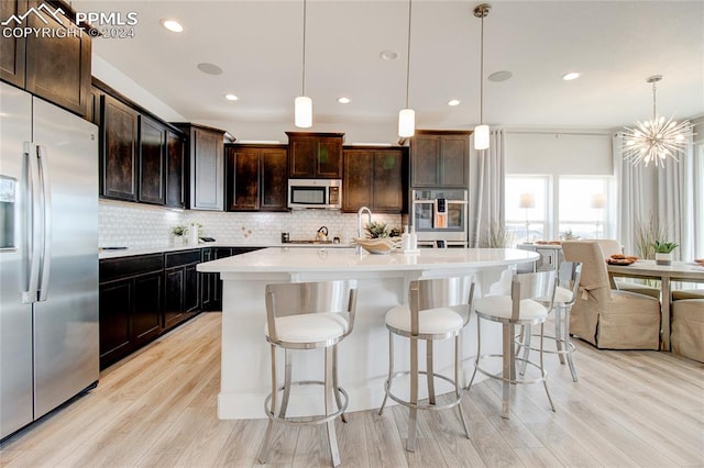 kitchen featuring a kitchen island with sink, hanging light fixtures, light wood-type flooring, appliances with stainless steel finishes, and dark brown cabinetry