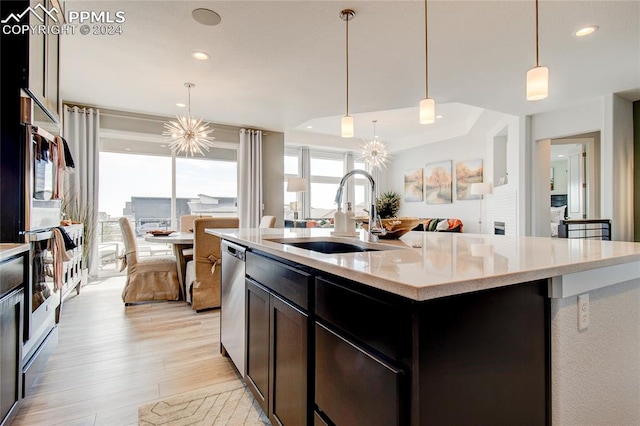 kitchen with sink, decorative light fixtures, an inviting chandelier, light hardwood / wood-style floors, and an island with sink