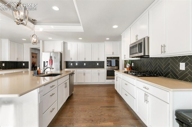 kitchen featuring appliances with stainless steel finishes, dark hardwood / wood-style flooring, a kitchen island with sink, white cabinetry, and hanging light fixtures